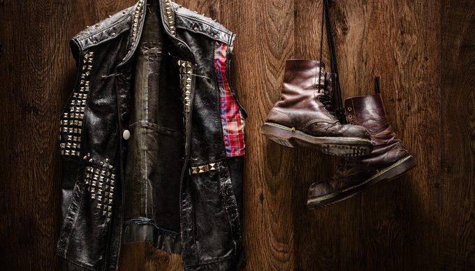 Punk-rock leather jacket and a pair of old boots hanging on a wooden wall